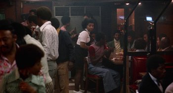 Movie still from “Mikey and Nicky” (1976), directed by Elaine May – A group of people standing and sitting around a table; Wide shot, Over the shoulder angle
