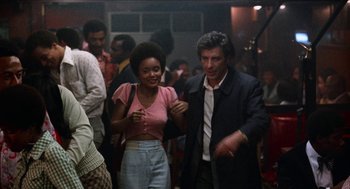Movie still from “Mikey and Nicky” (1976), directed by Elaine May – A man and a woman are standing in a crowd; Medium shot, Over the shoulder angle