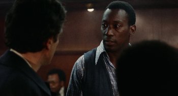 Movie still from “Mikey and Nicky” (1976), directed by Elaine May – A man standing next to another man in front of a crowd; Close Up shot, Over the shoulder angle