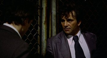 Movie still from “Mikey and Nicky” (1976), directed by Elaine May – A man wearing a suit and tie next to a fence; Close Up shot, Over the shoulder angle