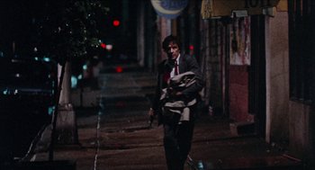 Movie still from “Mikey and Nicky” (1976), directed by Elaine May – A man walking down a street holding a gun; Wide shot, Low angle
