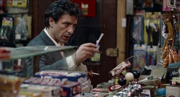 Movie still from “Mikey and Nicky” (1976), directed by Elaine May – A man sitting in front of a table holding a cell phone; Medium shot, Over the shoulder angle