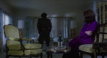 Movie still from “Mikey and Nicky” (1976), directed by Elaine May – A man standing in front of a table with a wine bottle on top of it; Medium shot, Over the shoulder angle