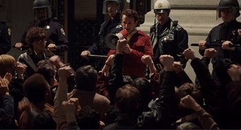 Movie still from “Milk” (2008), directed by Gus Van Sant – A group of people standing around a crowd of people; Medium shot, High angle