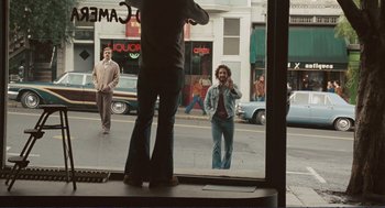Movie still from “Milk” (2008), directed by Gus Van Sant – A man standing in front of a window on a street; Wide shot, Over the shoulder angle