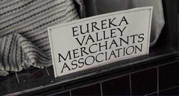 Movie still from “Milk” (2008), directed by Gus Van Sant – A black and white photo of a sign that reads " eureka valley merchant association "; Medium shot, Overhead angle