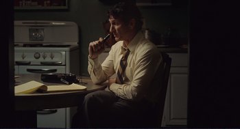Movie still from “Milk” (2008), directed by Gus Van Sant – A man sitting at a table in a room; Medium shot, Low angle