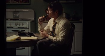 Movie still from “Milk” (2008), directed by Gus Van Sant – A man sitting at a table with a tie around his mouth; Medium shot, Over the shoulder angle