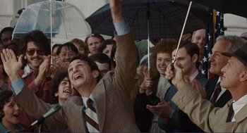 Movie still from “Milk” (2008), directed by Gus Van Sant – A crowd of people are gathered around a man holding an umbrella; Medium shot, High angle