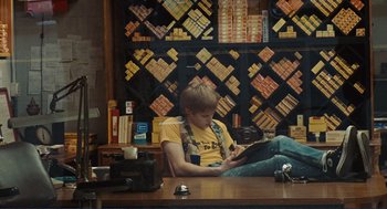 Movie still from “Milk” (2008), directed by Gus Van Sant – A person sitting at a table with a camera; Wide shot, Over the shoulder angle