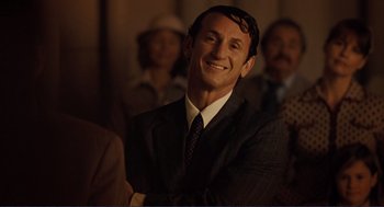 Movie still from “Milk” (2008), directed by Gus Van Sant – A man in a suit and tie smiling for the camera; Close Up shot, Over the shoulder angle