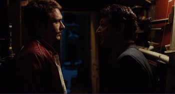 Movie still from “Milk” (2008), directed by Gus Van Sant – Two men standing next to each other in a dark room; Medium shot, Over the shoulder angle