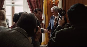 Movie still from “Milk” (2008), directed by Gus Van Sant – Two men in suits shaking hands in front of a camera; Medium shot, Over the shoulder angle