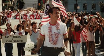 Movie still from “Milk” (2008), directed by Gus Van Sant – A group of people marching down a street with american flags; Medium shot, High angle