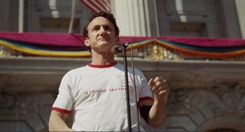 Movie still from “Milk” (2008), directed by Gus Van Sant – A man standing in front of a microphone on a stage; Medium shot, Low angle