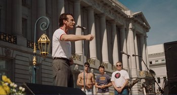 Movie still from “Milk” (2008), directed by Gus Van Sant – A man speaking into a microphone on a stage; Medium shot, Low angle