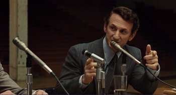 Movie still from “Milk” (2008), directed by Gus Van Sant – A man in a business suit is speaking into a microphone; Close Up shot, Over the shoulder angle