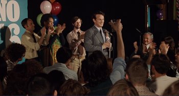 Movie still from “Milk” (2008), directed by Gus Van Sant – A group of people on a stage holding microphones; Medium shot, Over the shoulder angle