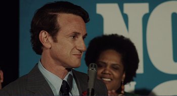 Movie still from “Milk” (2008), directed by Gus Van Sant – A person speaking at a microphone; Close Up shot, Over the shoulder angle