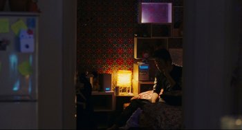 Movie still from “Millennium Mambo” (2001), directed by Hsiao-Hsien Hou – A man sitting on top of a bed reading a book; Wide shot, High angle