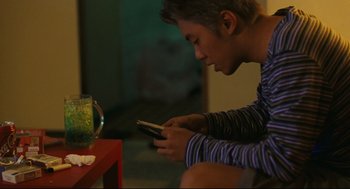 Movie still from “Millennium Mambo” (2001), directed by Hsiao-Hsien Hou – A man sitting on the ground looking at his cell phone; Medium shot, Low angle
