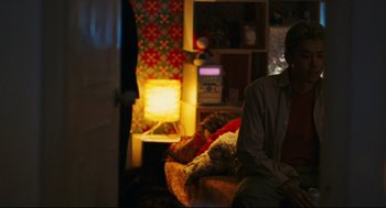 Movie still from “Millennium Mambo” (2001), directed by Hsiao-Hsien Hou – A man sitting on a couch in a living room; Medium shot, Over the shoulder angle
