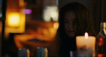Movie still from “Millennium Mambo” (2001), directed by Hsiao-Hsien Hou – A woman with long dark brown hair is sitting at a table with a candle; Close Up shot, Over the shoulder angle