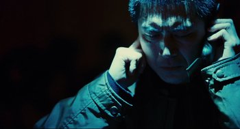 Movie still from “Millennium Mambo” (2001), directed by Hsiao-Hsien Hou – A man in a dark room holding his hand to his ear; Close Up shot, Over the shoulder angle