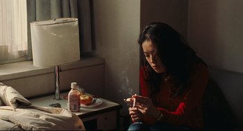 Movie still from “Millennium Mambo” (2001), directed by Hsiao-Hsien Hou – A woman smoking a cigarette while sitting at a table; Medium shot, High angle