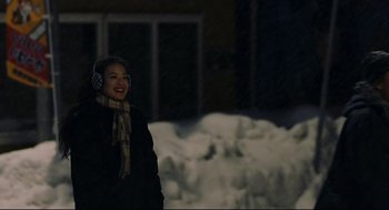 Movie still from “Millennium Mambo” (2001), directed by Hsiao-Hsien Hou – A person wearing ear muffs standing in front of a building; Medium shot, Over the shoulder angle