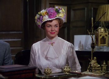 Movie still from “Million Dollar Mermaid” (1952), directed by Mervyn LeRoy – A woman wearing a floral hat sitting at a table; Medium shot, Over the shoulder angle