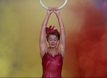 Movie still from “Million Dollar Mermaid” (1952), directed by Mervyn LeRoy – A woman in a red dress holding a hula hoop above her head; Medium shot, Low angle