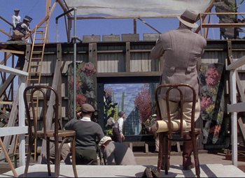 Movie still from “Million Dollar Mermaid” (1952), directed by Mervyn LeRoy – A man sitting on top of a chair in front of a tv; Wide shot, Low angle
