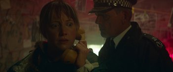 Movie still from “Mindhorn” (2016), directed by Sean Foley – A woman holding a phone up to her ear while a police officer looks on; Close Up shot, Low angle