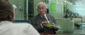 Movie still from “Mindhorn” (2016), directed by Sean Foley – An older man sitting at a table holding a container; Close Up shot, Over the shoulder angle