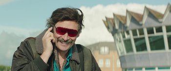 Movie still from “Mindhorn” (2016), directed by Sean Foley – A man with a mustache wearing sunglasses talking on a cell phone; Close Up shot, Low angle