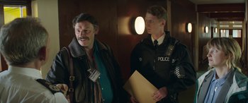 Movie still from “Mindhorn” (2016), directed by Sean Foley – Two police officers standing next to each other in a room; Medium shot, Over the shoulder angle