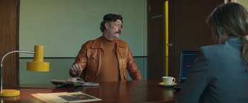 Movie still from “Mindhorn” (2016), directed by Sean Foley – A man sitting at a wooden table with a cup of coffee; Medium shot, Over the shoulder angle