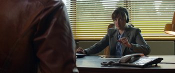 Movie still from “Mindhorn” (2016), directed by Sean Foley – A person sitting at a table with a phone; Medium shot, Over the shoulder angle