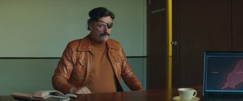 Movie still from “Mindhorn” (2016), directed by Sean Foley – A man wearing a brown leather jacket sitting at a table; Medium shot, Over the shoulder angle