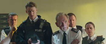 Movie still from “Mindhorn” (2016), directed by Sean Foley – Three men in police uniforms looking at a cell phone; Medium shot, Over the shoulder angle