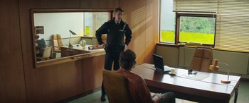 Movie still from “Mindhorn” (2016), directed by Sean Foley – A police officer talking to a man sitting in front of a computer; Medium shot, Over the shoulder angle
