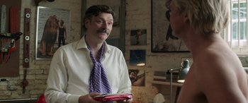 Movie still from “Mindhorn” (2016), directed by Sean Foley – A man in a white dress shirt and purple tie holding a pink box; Medium shot, Over the shoulder angle