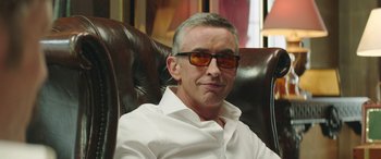 Movie still from “Mindhorn” (2016), directed by Sean Foley – A person sitting in a chair wearing sunglasses; Close Up shot, Low angle