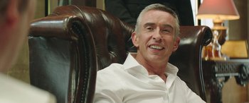 Movie still from “Mindhorn” (2016), directed by Sean Foley – A man sitting in a chair smiling for the camera; Close Up shot, Over the shoulder angle