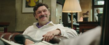Movie still from “Mindhorn” (2016), directed by Sean Foley – A man sitting in a chair with his hands on his chest; Close Up shot, Over the shoulder angle