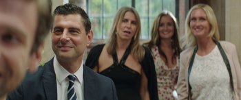 Movie still from “Mindhorn” (2016), directed by Sean Foley – A group of people standing next to each other in front of a window; Close Up shot, Over the shoulder angle