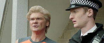 Movie still from “Mindhorn” (2016), directed by Sean Foley – A man with a blonde wig talking to a police officer; Close Up shot, Over the shoulder angle