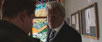 Movie still from “Mindhorn” (2016), directed by Sean Foley – An older man wearing a suit and tie in front of a window; Close Up shot, Over the shoulder angle