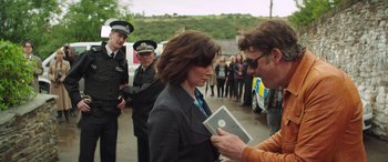 Movie still from “Mindhorn” (2016), directed by Sean Foley – A woman holding a book in front of a group of police officers; Medium shot, Over the shoulder angle